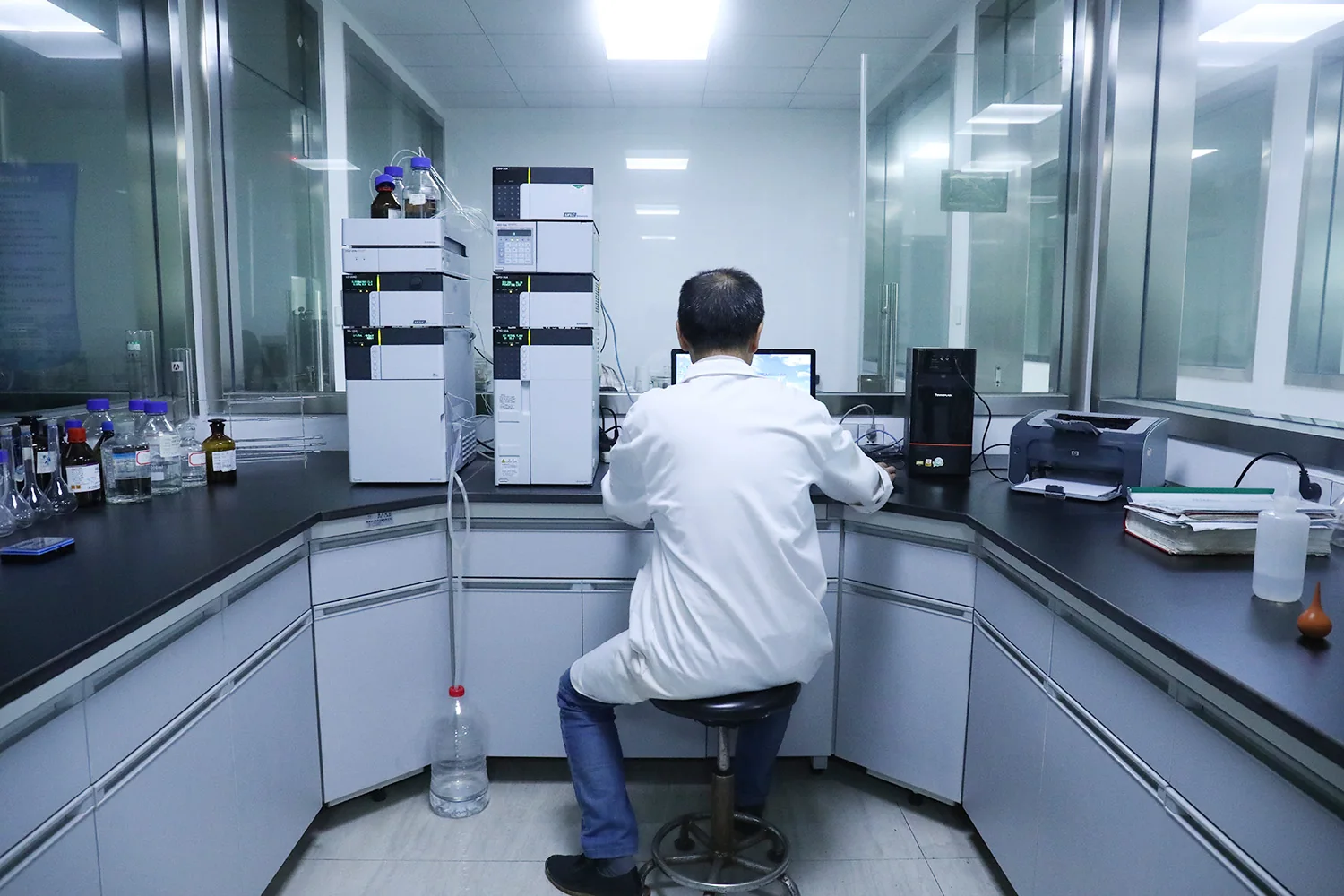 A laboratory technician seated at liquid chromatography equipment.